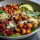 Close-up of a Buddha Bowl featuring fluffy quinoa, caramelized sweet potatoes, crunchy chickpeas, avocado, and a drizzle of garlicky tahini dressing.  