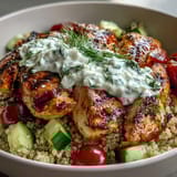 A close-up of a colorful Greek Chicken Power Bowl, featuring tender marinated chicken, quinoa, and a generous dollop of cool, garlicky tzatziki.