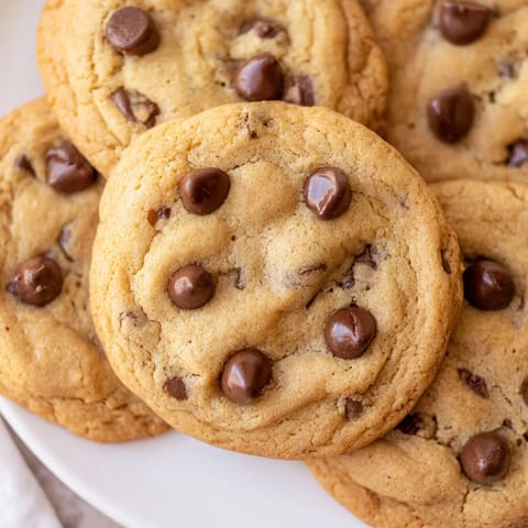 A close-up of Chocolate Chip Cookies with soft centers, arranged with a cold glass of milk.