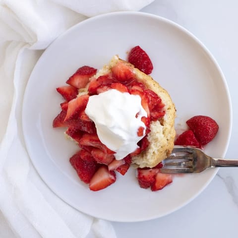 A rustic slice of Strawberry Shortcake reveals fluffy biscuit layers, macerated strawberries dripping with syrup, and a generous dollop of whipped cream.