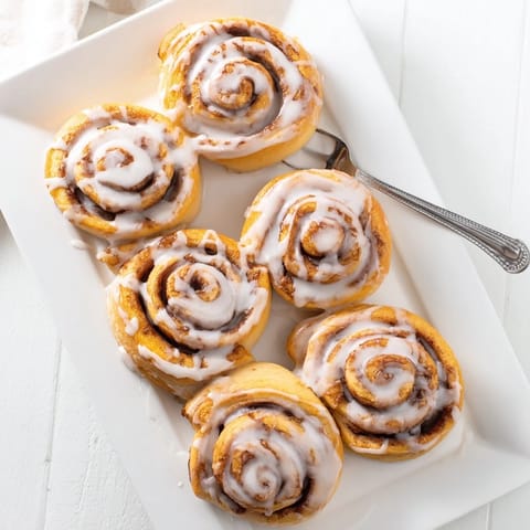Warm Cinnamon Rolls on a white plate, topped with creamy icing, ideal for a sweet breakfast or brunch treat.