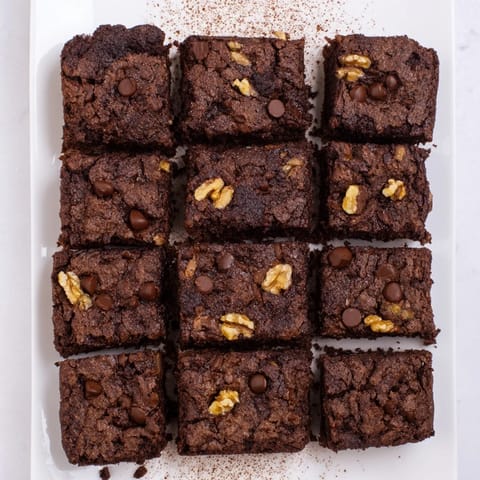 A close-up of rich brownies squares garnished with chocolate chips and walnuts.