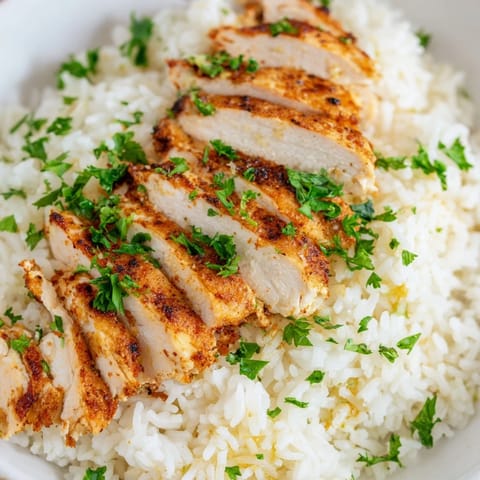 A serving of garlic butter rice with tender sliced chicken, featuring aromatic herbs and a rich, buttery texture in a comforting bowl.