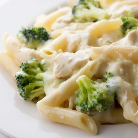 Chicken Broccoli Cheddar Pasta is served warm in a skillet, garnished with extra shredded sharp cheddar and herbs.  
