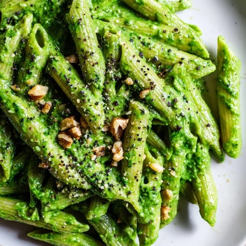 A vibrant plate of creamy spinach walnut pasta beside fresh spinach leaves and golden toasted walnuts.  