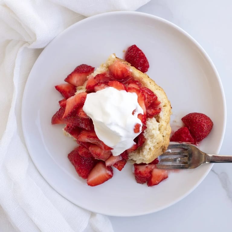 A rustic slice of Strawberry Shortcake reveals fluffy biscuit layers, macerated strawberries dripping with syrup, and a generous dollop of whipped cream.