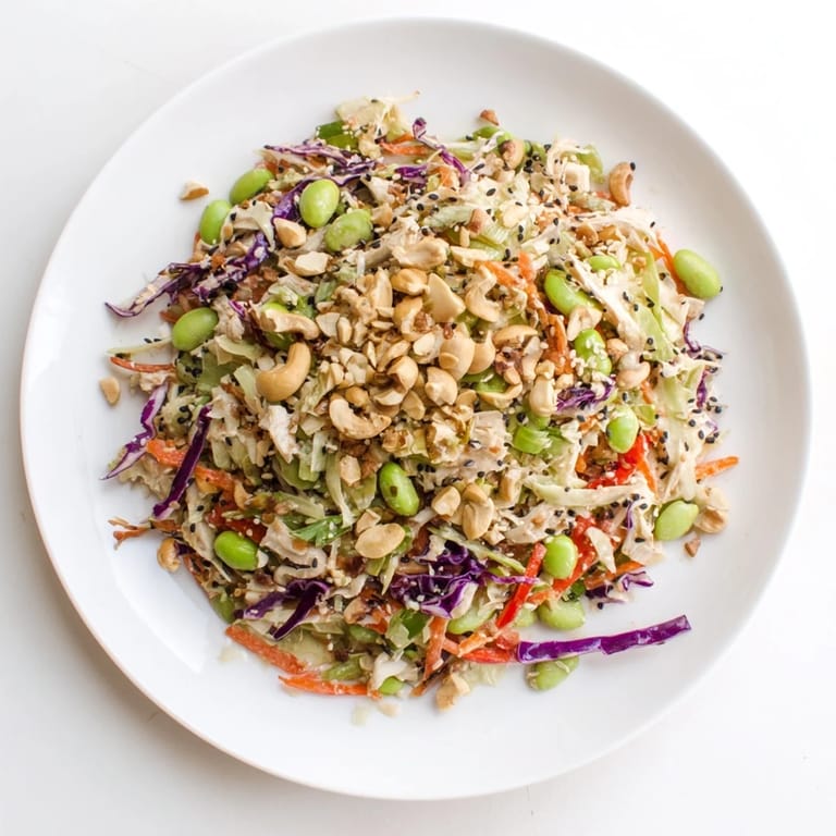 A colorful bowl of Edamame Crunch Chicken Salad, garnished with cashews and sliced red bell peppers.